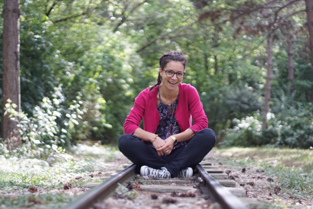 Strömerin Barbara Weißensteiner sitzt auf Bahngeleise einer Miniaturbahn und lacht im Hintergrund Wald