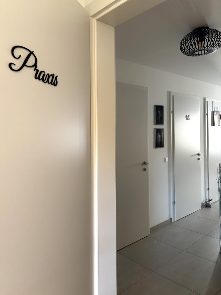 Weißer Flur mit weißen Türen in die Ström-Praxis mit Türschild Praxis