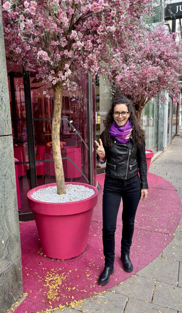 Barbara Weißensteiner stehend in schwarzer Kleidung im Hintergrund zwei große pinke Blumentöpfe mit rosa Kunstbäumen drin